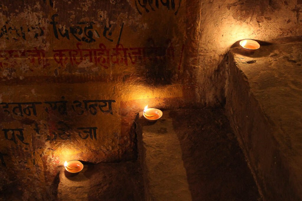 Photographie d’art contemporaine prise en Inde dans la cité sacrée de Varanasi ( Bénarès ). Tirage photographique fine art à vendre en édition limité et signé de l'artiste Magali Sacau. Cette œuvre photographique poétique représente trois lampes à huile déposée dans la nuit sur les marches des quais du Gange lors d'une cérémonie hindoue en signe de prière. Les lumières des bougies éclairent le mur peint en jaune et pourpre avec des écritures en sanskrit. La peinture du mur s'effrite. Cette photographie d’art pour décoration murale, idéale pour un intérieur élégant, ou pour favoriser le bien-être au travail d'une entreprise, séduira les collectionneurs d'art par ses jeux d'ombres et lumières sur les marches qui accentuent le côté spirituel de l'oeuvre. Les galeries d’art contemporaines intéressées par la spiritualité, l'Inde et les Lumières seront inspirées par cette photographie des Marches Sacrées.