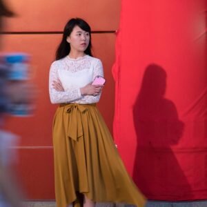 Cette photographie d’art éditée en tirages limités mise en vente, est le portrait d'une femme asiatique élégante et rêveuse. Cette œuvre poétique épurée sur fond de mur rouge qui contraste avec les touches de couleurs blanc, beige, et noir de la silhouette crée un effet très pictural. Cette photographie humaniste d'une élégante japonaise qui attend en rêvant dans le couloir du métro de Tokyo touchera les galeries comme les amateurs d'art par l'intemporalité de sa pause. Seule la présence de son téléphone portable à la main contraste avec l'intemporalité suggérée par la tenue en dentelle et la jupe fluide. Ce tableau photographique humaniste offrira l'évasion vers un ailleurs empli de douceur à son acquéreur, comme aux spectateurs lors d'une exposition.
