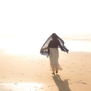 Photographie d’art humaniste contemporaine d'une silhouette féminine en robe en dentelle banche avec un voile bleu sur le haut de la tête et les épaule, qui court de dos sur le sable d'une plage océane. Cette œuvre photographique poétique signée de l'artiste, éditée en tirage limité ouvre une fenêtre sur un monde lumineux ou le souffle divin semble jaillir des pas de la jeune femme. Le papier fine art de cette photographie d'art met en valeur la profondeur du tableau et laisse s'en dégager une spiritualité intense. Une œuvre qui touche les cœurs à exposer chez les particuliers comme en galerie d’art contemporaine.