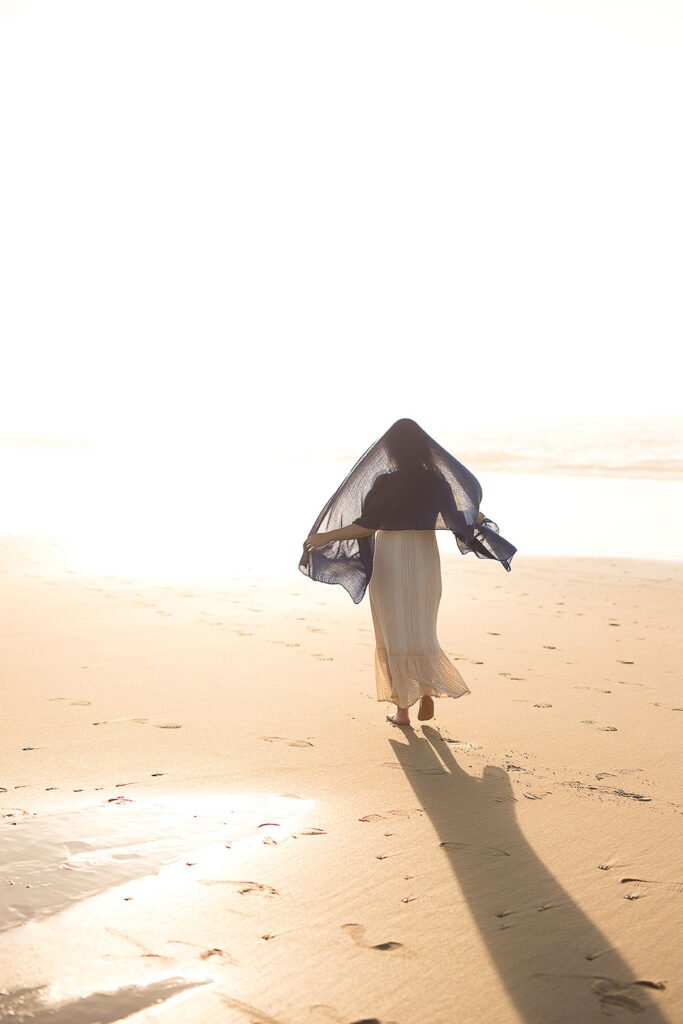 Photographie d’art humaniste contemporaine d'une silhouette féminine en robe en dentelle banche avec un voile bleu sur le haut de la tête et les épaule, qui court de dos sur le sable d'une plage océane. Cette œuvre photographique poétique signée de l'artiste, éditée en tirage limité ouvre une fenêtre sur un monde lumineux ou le souffle divin semble jaillir des pas de la jeune femme. Le papier fine art de cette photographie d'art met en valeur la profondeur du tableau et laisse s'en dégager une spiritualité intense. Une œuvre qui touche les cœurs à exposer chez les particuliers comme en galerie d’art contemporaine.