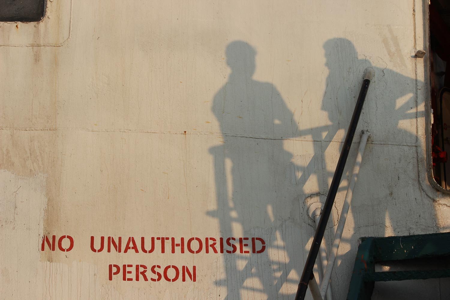 Photographie d'art humaniste dont le titre est Ensemble là-bas. Les ombres de deux silhouettes masculines sont en conversation sur le pont d'un vieux navire. La peinture blanche du bateau s'écaille, elle a des traces de rouille et un écriteau peint en rouge interdisant l'accès. Cette œuvre photographique revêt une tonalité humoristique puisque l'ombre des personnes se projette sur la passerelle interdite. Ce tirage d'art en édition limité a une tonalité intemporelle et irréelle dû à la luminosité du soleil couchant qui interpellera les amateurs d'art, les collectionneur comme les galeries d'art.
